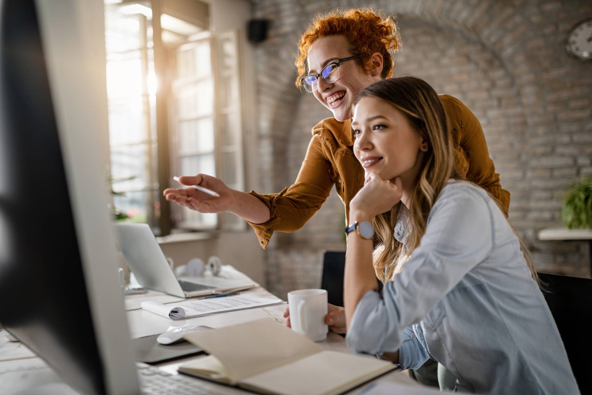 happy female entrepreneurs reading email computer while working together office focus is redhead woman1